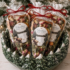 May include: Three clear cone-shaped plastic bags filled with a dried Christmas Tree Farm simmer blend of pine needles, dried flowers, and spices, tied with red string, resting in a dark green ceramic bowl with a molded pine tree rim design.