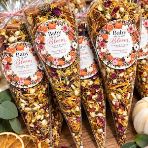 May include: Clear cone-shaped bags filled with a dried simmer blend of orange slices, cinnamon sticks, flower petals, and herbs. Each bag features a round label with the text Baby in Bloom Simmer Blend and is tied at the top with pink twine.