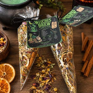 May include: Two clear cone-shaped plastic bags filled with a dried botanical simmer pot blend labeled Witches Brew. The contents include dried citrus slices, cinnamon sticks, and various herbs. Each bag features a dark green tag with white text.