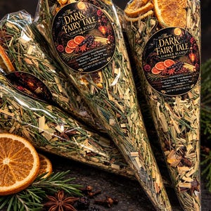 May include: Clear cone-shaped bags filled with The Dark Fairy Tale simmer blend, containing dried orange slices, blueberries, cloves, star anise, rosemary, and lemongrass. Each bag features a circular label with the product name and net weight 2.0 oz.