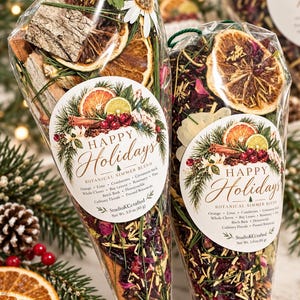 May include: Two clear cone-shaped bags filled with a botanical simmer blend. Each bag features a label reading Happy Holidays Botanical Simmer Blend, listing ingredients like orange, lime, cranberries, cinnamon, and pine. Net weight 3.0 oz.