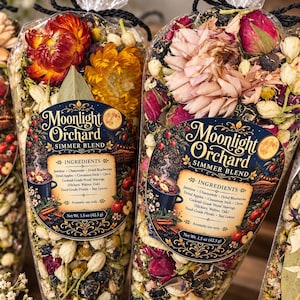 May include: Two clear cone-shaped bags filled with dried botanicals, including red and yellow flowers, berries, and wood shavings. Each bag features a Moonlight Orchard Simmer Blend label listing ingredients like jasmine, chamomile, and dried apples, with a net weight of 1.5 oz (42.5 g).