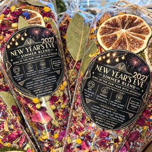 May include: Clear plastic cone-shaped bags filled with a New Year's Eve 2027 simmer blend. The mixture contains dried orange slices, bay leaves, rose petals, lavender, and chamomile. A black circular label features gold text and fireworks.