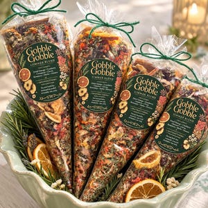 May include: Four clear cone-shaped bags filled with a dried potpourri simmer blend of orange slices, cranberries, cinnamon, and herbs. Each bag features a dark green label reading Gobble Gobble Simmer Blend and is tied with a green string.