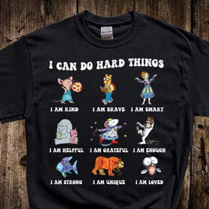 May include: Black t-shirt with the text "I CAN DO HARD THINGS" and illustrations of cartoon characters. Below each character is a positive affirmation: "I AM KIND," "I AM BRAVE," "I AM SMART," "I AM HELPFUL," "I AM GRATEFUL," "I AM ENOUGH," "I AM STRONG," "I AM UNIQUE," and "I AM LOVED."