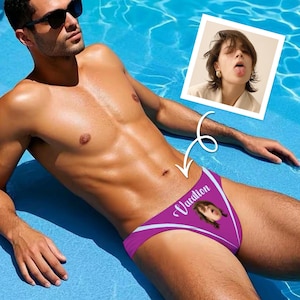 May include: A purple swimsuit bottom featuring a white graphic of a person with their tongue out and the word Vacation printed in white script. The swimsuit has white accent lines and is displayed on a person in a bright blue swimming pool.