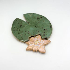 以下が含まれることがあります： セラミック製の睡蓮の葉と花の彫刻。 睡蓮の葉は、濃い斑点のあるまだら模様の緑色です。 花は、白い中心部を持つ明るいピーチ色です。