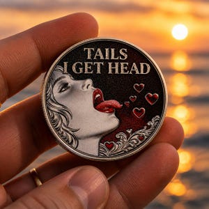 Può includere: Una moneta d'argento con la scritta "TAILS I GET HEAD" e l'illustrazione di una donna con la lingua di fuori. La moneta ha un bordo decorativo e cuori. La moneta è tenuta in una mano.