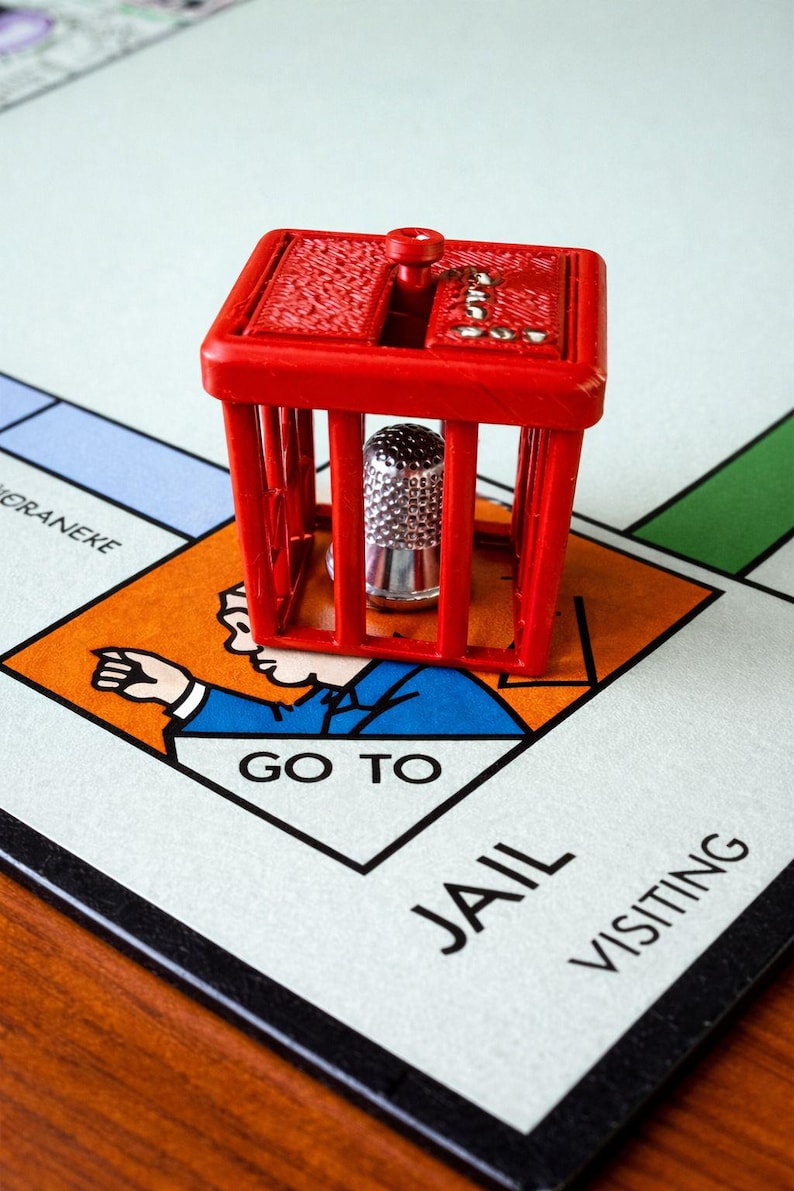 Pu&ograve; includere: Una cella di prigione di plastica rossa con un ditale d'argento all'interno, appoggiata su un tabellone di gioco del Monopoli. Il tabellone mostra lo spazio "Vai in prigione". Il pezzo del gioco &egrave; un elemento classico del gioco.