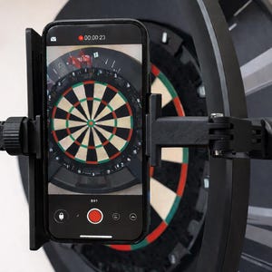 Może przedstawiać: Czarny smartfon jest zamontowany na czarnym uchwycie, ustawionym przed tarczą do darta. Telefon wyświetla nagranie na żywo tarczy, z widocznym czerwonym przyciskiem nagrywania. Tarcza do darta ma klasyczny design z czerwonymi, zielonymi i białymi segmentami.