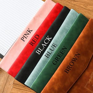 May include: A collection of leather-like notebook covers in pink, red, black, blue, green, and brown. Each cover has a different color and the color name printed on it. A lined notepad is visible on the left.