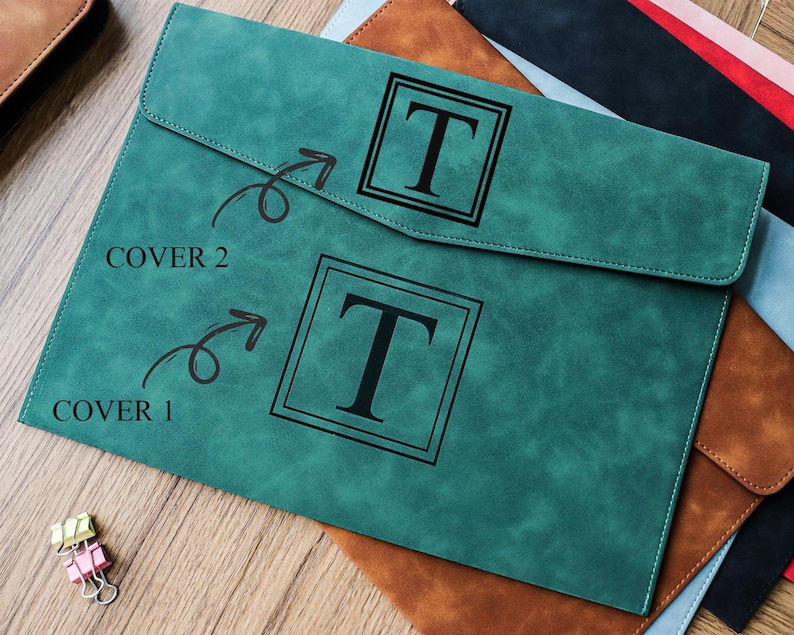 May include: A teal-colored document folder with a flap closure, featuring a large black letter "T" within a square frame. The text "COVER 1" and "COVER 2" are visible. Other folders in brown, black, and blue are partially visible.