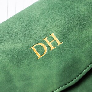 May include: Close-up of a green leather item with gold-colored initials "DH". The item has a textured surface and a stitched edge. The initials are centered and stand out against the green background.