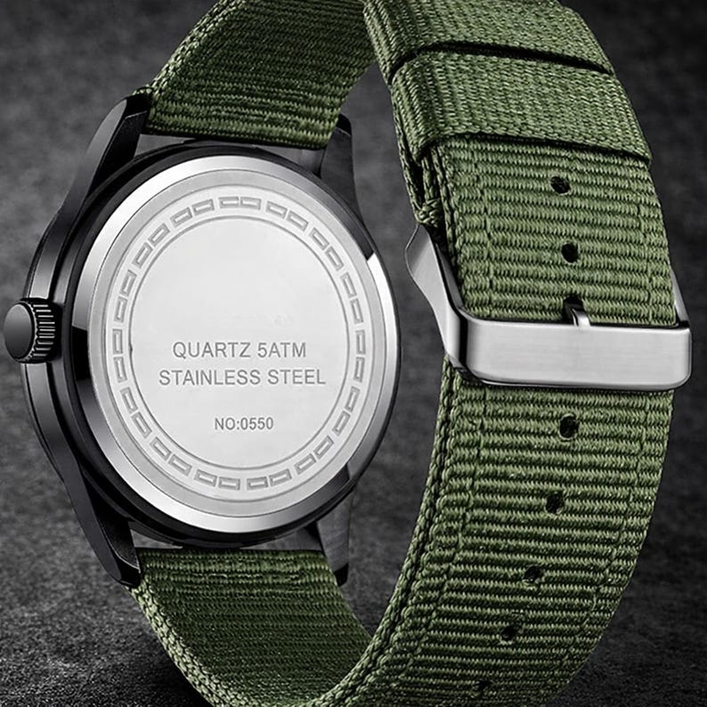 May include: Close-up of a black wristwatch with a green nylon strap. The watch face is silver with black hands and markers. The back of the watch is silver with the text "QUARTZ 5ATM STAINLESS STEEL" and "NO:0550".