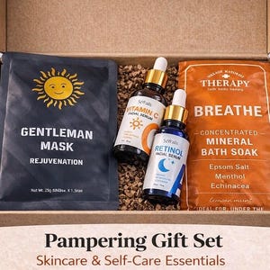 May include: A pampering gift set in a cardboard box. The set includes a black face mask with a sun graphic, two facial serum bottles, and an orange bath soak packet. The box is filled with brown packing material. Text on the box reads "Pampering Gift Set Skincare & Self-Care Essentials."