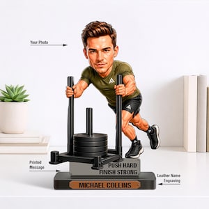 May include: A figurine of a man pushing a weight sled, with the text "PUSH HARD FINISH STRONG" and a nameplate that reads "MICHAEL COLLINS". The man is wearing a green shirt and black shorts. A succulent plant in a white pot is on the left.