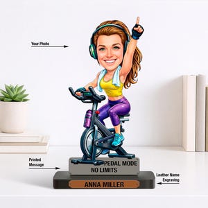 May include: A figurine of a woman on a stationary bike, wearing headphones and workout clothes. The figurine has a yellow top, purple leggings, and blue sneakers. The base has the text "PEDAL MODE NO LIMITS" and "ANNA MILLER".