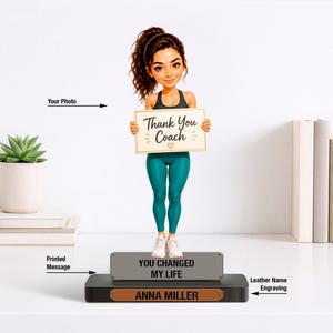 May include: A custom bobblehead figurine of a person with a ponytail wearing a black tank top and teal leggings, holding a sign that reads Thank You Coach. The base features a grey plaque with the text YOU CHANGED MY LIFE and a brown nameplate.