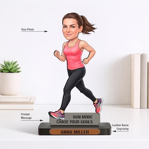 May include: A cartoon figurine of a woman running, wearing a pink tank top and black leggings. The figurine is on a black base with the text "RUN MODE CHASE YOUR GOALS" and the name "ANNA MILLER". A succulent plant in a white pot is to the left.