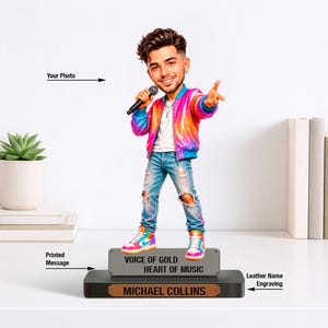 Könnte beinhalten: Eine personalisierte Wackelkopf-Figur einer Person mit Mikrofon, bekleidet mit einer leuchtend pink-orangen Jacke, weißem T-Shirt, zerrissener blauer Jeans und bunten Turnschuhen. Der Sockel trägt den Text "VOICE OF GOLD HEART OF MUSIC" und "MICHAEL COLLINS".
