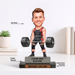 May include: A custom bobblehead figure of a person lifting a barbell, wearing a black and red singlet with knee sleeves. The base features a grey plaque with the text "STRONG MAN IN ACTION" and a brown leather nameplate reading "MICHAEL COLLINS".