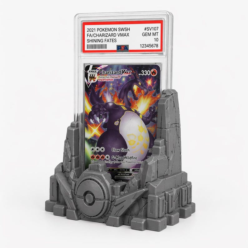 May include: A graded Pok&eacute;mon card featuring Charizard VMAX, displayed in a clear case. The card is set in a gray, stylized stone display stand. The card's details include the text "2021 POKEMON SWSH FA/CHARIZARD VMAX SHINING FATES".