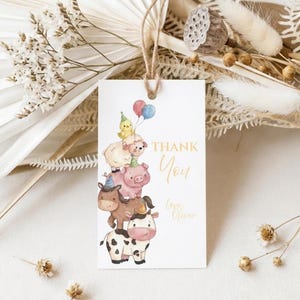 May include: A white gift tag with a watercolor illustration of stacked farm animals, including a cow, donkey, pig, sheep, and chick holding balloons. The tag reads "Thank You" in gold script, with a space for a name.