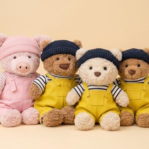 May include: Four plush toys including one pig and three bears, each wearing a striped shirt, solid-colored overalls, and a knit beanie. The pig wears pink, while the bears wear yellow overalls with navy blue beanies, all featuring soft fur.