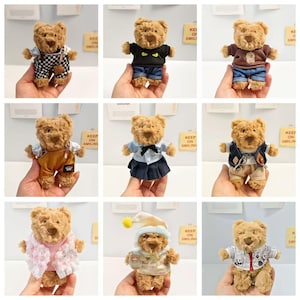 May include: A collection of nine small plush teddy bears, each wearing different miniature outfits including overalls, sweaters, skirts, and jackets. The bears have brown fur, dark eyes, and stitched noses, displayed in various clothing styles.