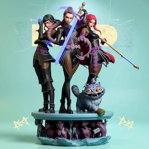 May include: A detailed figurine featuring three female characters in black and purple outfits, each holding a weapon. A gray cat with yellow eyes sits at the base of the figurine. The base has a light blue color with small figures around the base.