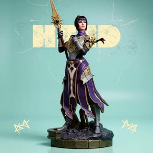 Puede incluir: Figura detallada de una guerrera con armadura plateada y dorada, sosteniendo una lanza con un emblema solar. Lleva una falda morada y dorada y está sobre una base de piedra. El fondo es de color turquesa claro con la palabra "HERO" en amarillo descolorido.