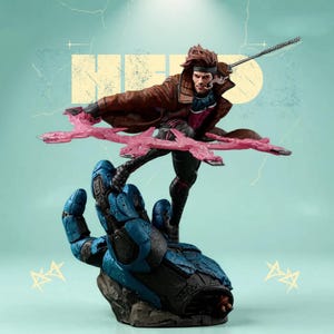 Può includere: Una statuetta dettagliata del personaggio dei fumetti Marvel, Gambit. La figura è in una posa dinamica, con un cappotto marrone, un abito nero e viola ed effetti energetici rosa. La figura è montata su una base blu e grigia.