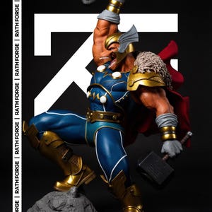 Op de afbeelding: Een gedetailleerd beeld van Thor in een dynamische pose, met een hamer. Het figuur draagt een blauw en goud kostuum met een rode cape. Het beeld staat op een rotsachtige basis, met de tekst "RATH FORGE".
