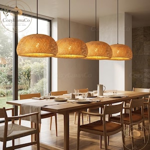 May include: Four woven rattan pendant lights hang above a long wooden dining table set for a meal. The lights are round, with a warm, natural color. The table is surrounded by wooden chairs.