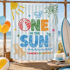 May include: A rectangular fabric backdrop featuring light blue and white vertical stripes with the text "ONE IN THE SUN" and "CAMDEN'S 1ST BIRTHDAY" in colorful, crayon-style lettering, decorated with illustrations of a sun, palm tree, and beach chair.