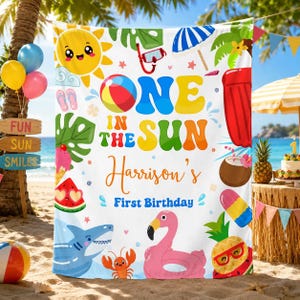 May include: A white rectangular backdrop featuring colorful summer graphics including a smiling sun, beach ball, snorkel, watermelon, shark, flamingo, and pineapple. The text reads "ONE IN THE SUN", "Harrison's", and "First Birthday" in vibrant, multi-colored lettering.