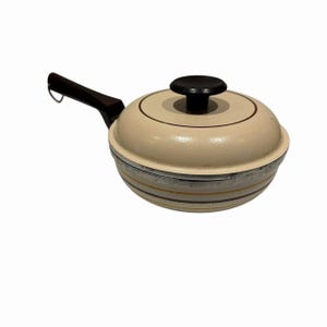 May include: A cream-colored saucepan with a matching domed lid and a dark brown handle. The lid features a dark brown circular knob and a thin brown ring detail. The base of the pan has horizontal brown stripes around the exterior surface.