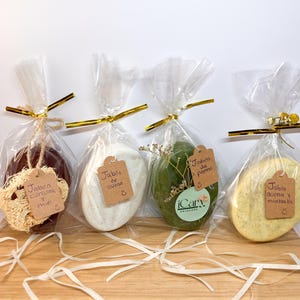 May include: Four wrapped soaps with tags. The soaps are in clear cellophane bags tied with gold ribbon. The tags read "Jabón curcuma y miel", "Jabón de avena", "Jabón de pepino", and "Jabón avena y manzanilla".