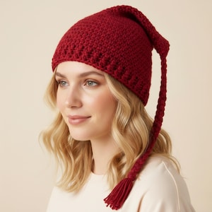 Può includere: Un cappello lavorato a maglia, rosso intenso, con una lunga coda intrecciata e nappa. Il cappello è in tinta unita e sembra fatto a mano. È un accessorio invernale.