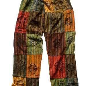 May include: Multi-coloured patchwork trousers with a drawstring waist. The colours include green, orange, red, and brown. The fabric is divided into rectangular patches and decorated with black floral designs.