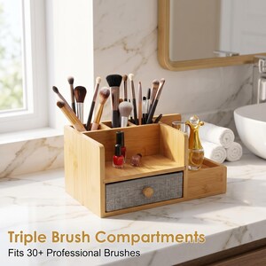 May include: A bamboo makeup organizer featuring multiple vertical compartments for brushes, a central open shelf, and a single gray fabric drawer with a round wooden knob. The unit holds various makeup brushes, nail polish bottles, and a gold-topped glass bottle.