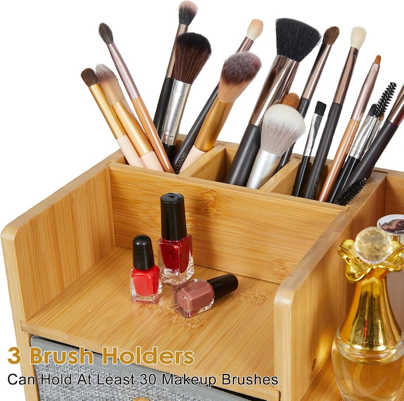 May include: A bamboo makeup organizer with multiple compartments containing various makeup brushes, three small nail polish bottles, and a gold-topped glass bottle. Text on the image reads: 3 Brush Holders, Can Hold At Least 30 Makeup Brushes.