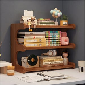 May include: A three-tiered wooden desk organizer shelf holding books, two yellow binders, a stack of colorful markers, a pink pig-shaped digital clock, a vintage-style record player, headphones, two small figurines, and a potted plant.