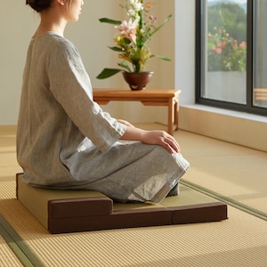 Pode incluir: Um conjunto de almofadas de meditação em tons de castanho e bege. O conjunto inclui uma base retangular e uma almofada menor. As almofadas são colocadas sobre um tapete de tatami, criando um espaço sereno e confortável para meditação e mindfulness.
