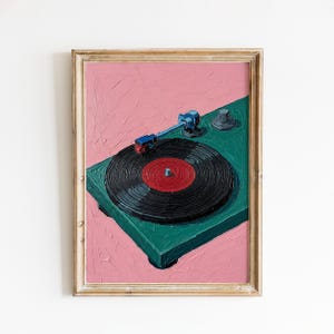 May include: A framed painting of a vintage record player. The turntable is teal, with a black record and a red center. The background is pink, and the frame is gold.