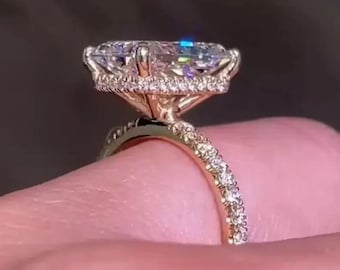 May include: Close-up of a gold ring with a large, clear, rectangular-cut gemstone. The band is encrusted with small, sparkling diamonds. The gemstone is surrounded by a halo of smaller diamonds.