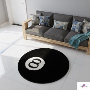 May include: A circular black rug featuring a white number eight design. The rug is placed on a white tiled floor, in front of a grey sofa with a wooden frame and patterned cushions. A blue throw is draped over the sofa.