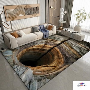 Op de afbeelding: Een rechthoekig vloerkleed met een 3D-afbeelding van een diep gat. Het kleed heeft tinten bruin, grijs en blauw, wat een realistisch, getextureerd effect creëert. Het kleed ligt in een woonkamer met een beige bank en decoratieve elementen.