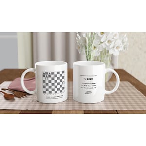 May include: Two white ceramic coffee mugs with black text and chess-themed graphics. One mug displays a chessboard and the text "WHITE TO MOVE! MATE IN 2". The other mug has chess move instructions.