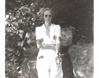 Haughty Woman Reluctantly Poses For Photo 1940’s Fashion White Jumpsuit Round Sunglasses Blonde-Haired Woman Smoking Cigarette